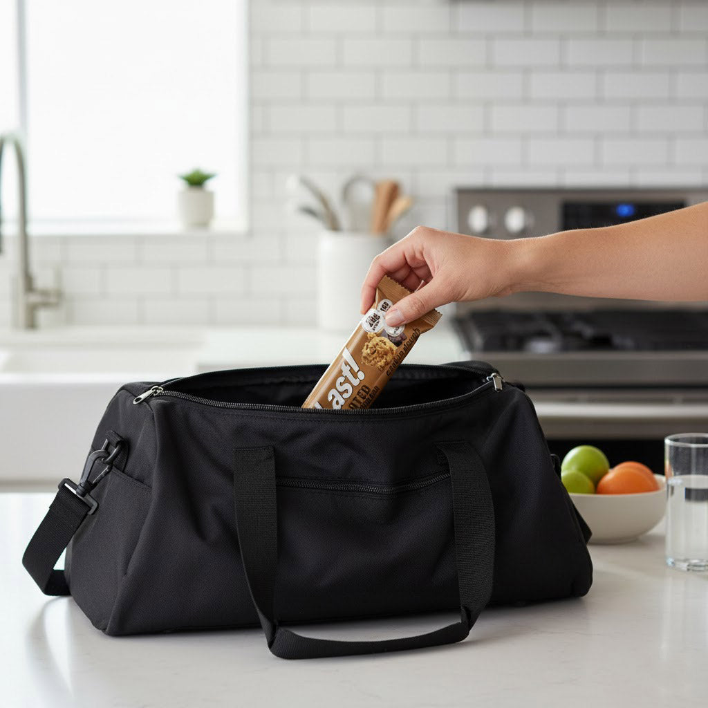 A hand pulling out an AtLast protein bar from a gym bag on a kitchen counter